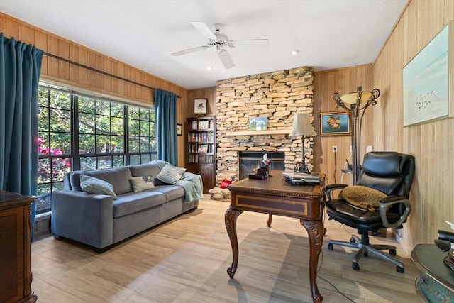 office area with ceiling fan, wood walls, and a stone fireplace