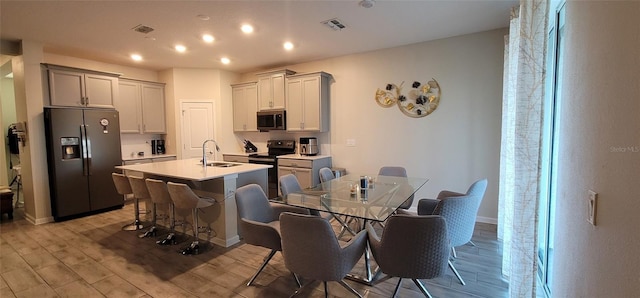 kitchen with sink, a breakfast bar area, a center island with sink, light hardwood / wood-style floors, and black appliances