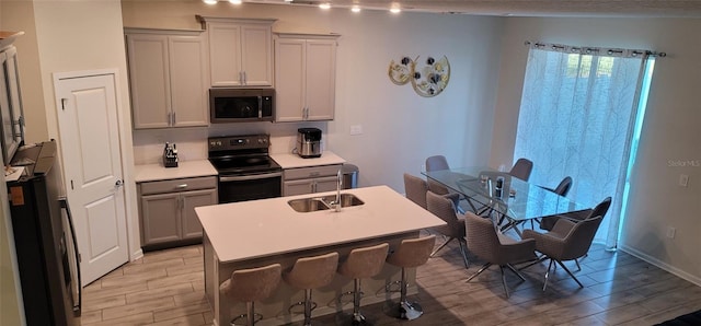 kitchen with a breakfast bar, sink, appliances with stainless steel finishes, gray cabinets, and an island with sink