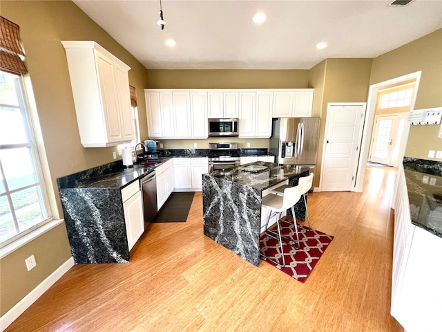 kitchen featuring white cabinets, sink, dark stone countertops, light wood-type flooring, and stainless steel appliances