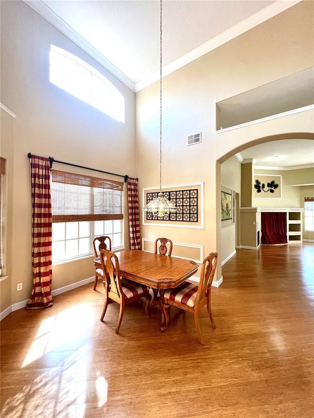 dining room with hardwood / wood-style flooring, a healthy amount of sunlight, a high ceiling, and ornamental molding