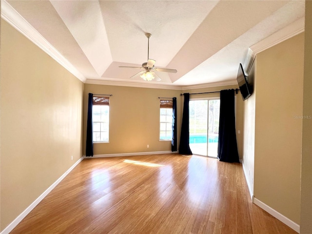 spare room with a tray ceiling, ceiling fan, light wood-type flooring, and ornamental molding