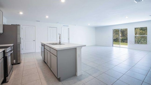 kitchen featuring appliances with stainless steel finishes, gray cabinetry, sink, light tile patterned floors, and an island with sink