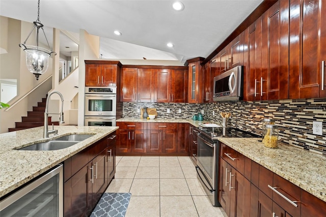 kitchen featuring sink, vaulted ceiling, light stone countertops, decorative light fixtures, and stainless steel appliances