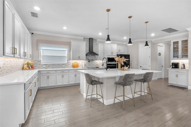 kitchen featuring white cabinetry, wall chimney exhaust hood, a breakfast bar area, and an island with sink