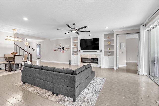 living room with crown molding, built in features, a stone fireplace, a textured ceiling, and ceiling fan with notable chandelier