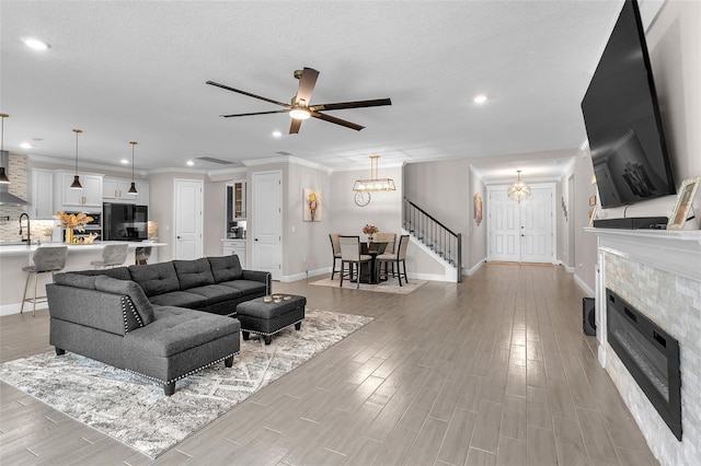 living room with ceiling fan with notable chandelier, a textured ceiling, sink, light hardwood / wood-style flooring, and a tiled fireplace