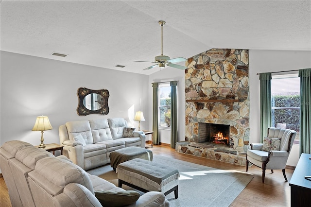 living room featuring ceiling fan, light hardwood / wood-style floors, a textured ceiling, lofted ceiling, and a fireplace