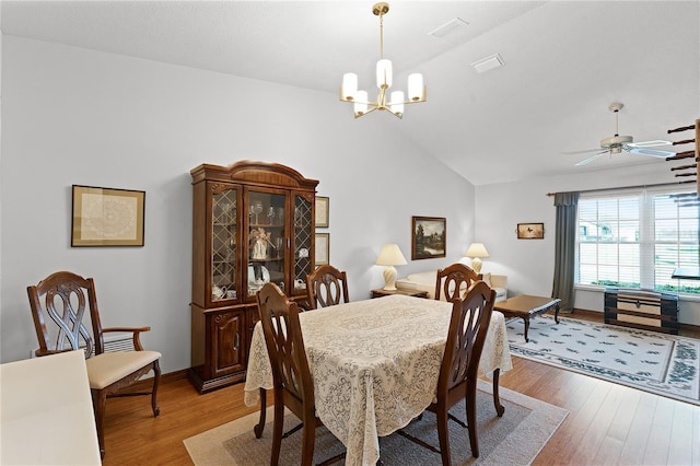 dining area featuring ceiling fan with notable chandelier, wood-type flooring, and vaulted ceiling