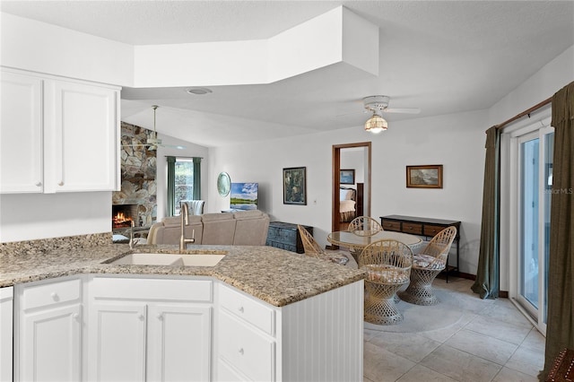 kitchen featuring white cabinets, sink, ceiling fan, a fireplace, and kitchen peninsula