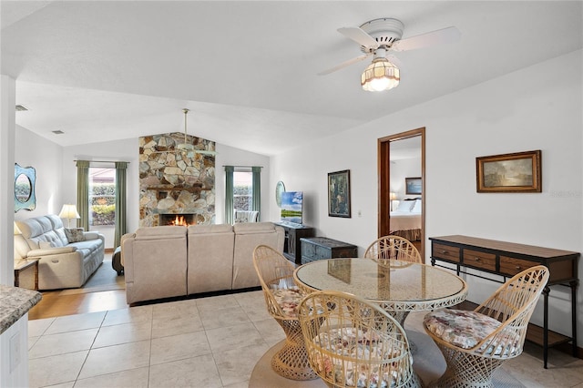 tiled dining area with vaulted ceiling, ceiling fan, and a stone fireplace