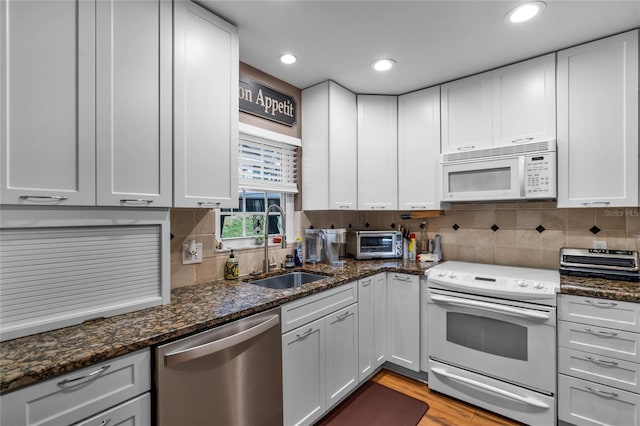 kitchen featuring sink, white appliances, light hardwood / wood-style flooring, white cabinets, and dark stone counters