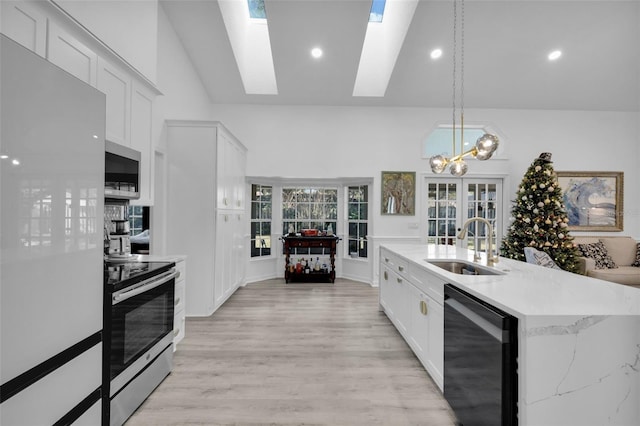 kitchen with white cabinets, stainless steel appliances, hanging light fixtures, and a skylight