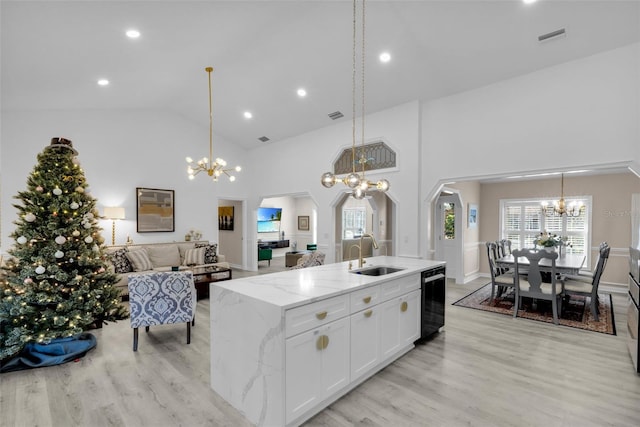 kitchen featuring light stone counters, a kitchen island with sink, sink, pendant lighting, and white cabinets