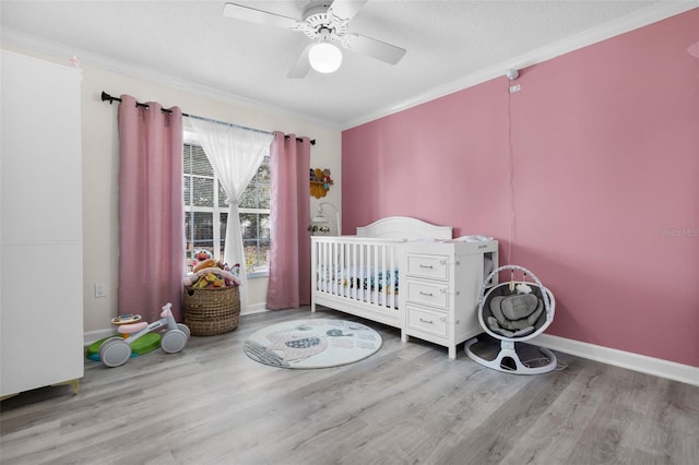 bedroom with light hardwood / wood-style flooring, a nursery area, ornamental molding, and ceiling fan