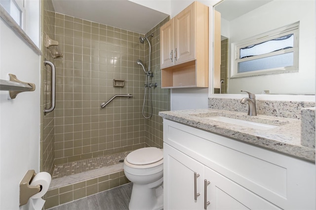 bathroom featuring a tile shower, hardwood / wood-style floors, vanity, and toilet