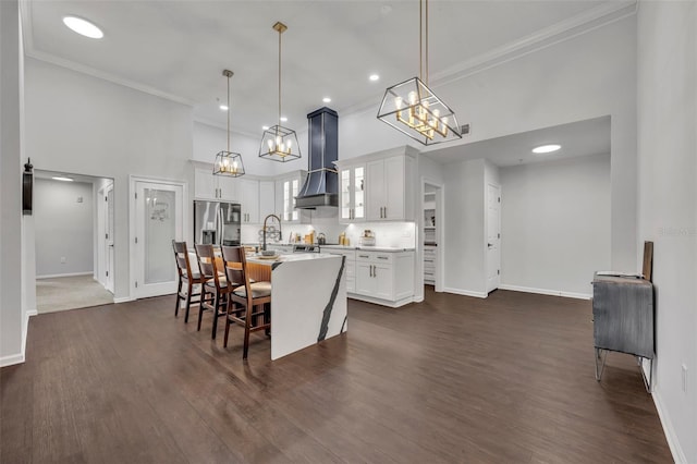 kitchen featuring a breakfast bar area, white cabinetry, an island with sink, decorative light fixtures, and custom exhaust hood