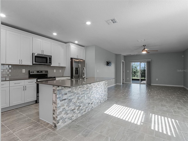 kitchen featuring white cabinets, ceiling fan, an island with sink, and stainless steel appliances