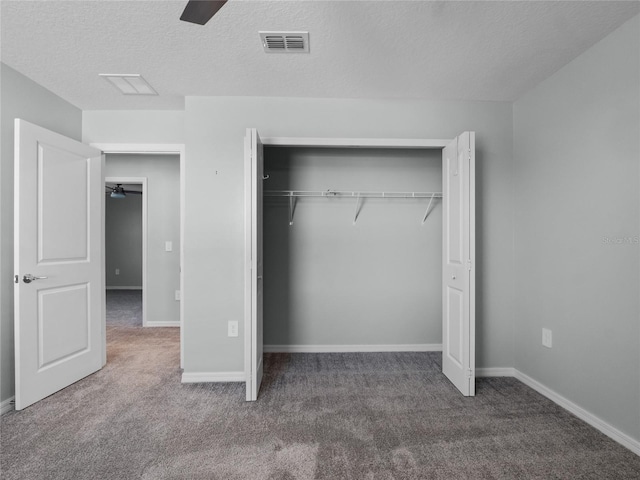 unfurnished bedroom featuring ceiling fan, a closet, a textured ceiling, and dark colored carpet