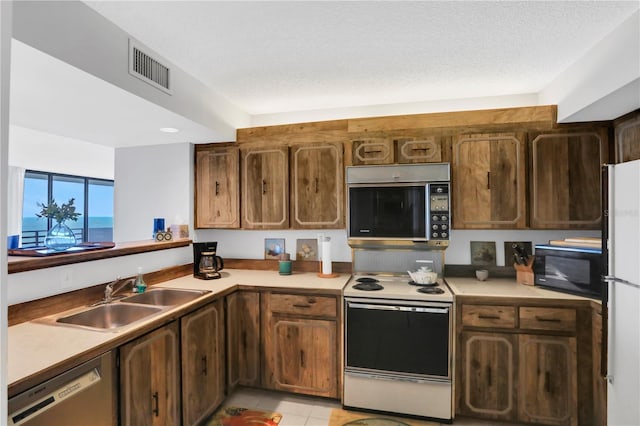 kitchen featuring a textured ceiling, white appliances, sink, and light tile patterned floors