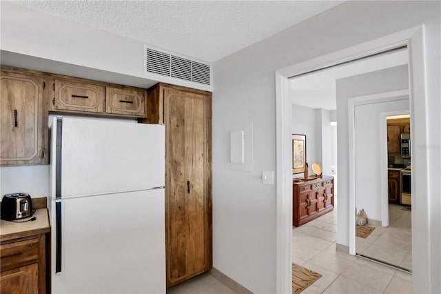 kitchen with range with electric cooktop, light tile patterned floors, a textured ceiling, and white refrigerator