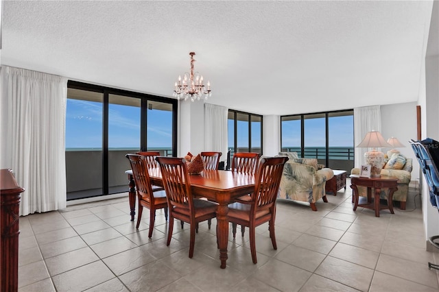 dining space featuring light tile patterned floors, a textured ceiling, a water view, and an inviting chandelier