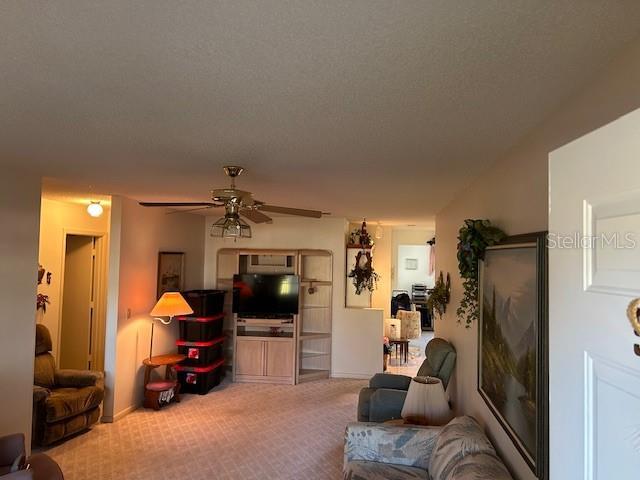 living room featuring carpet floors, ceiling fan, and a textured ceiling