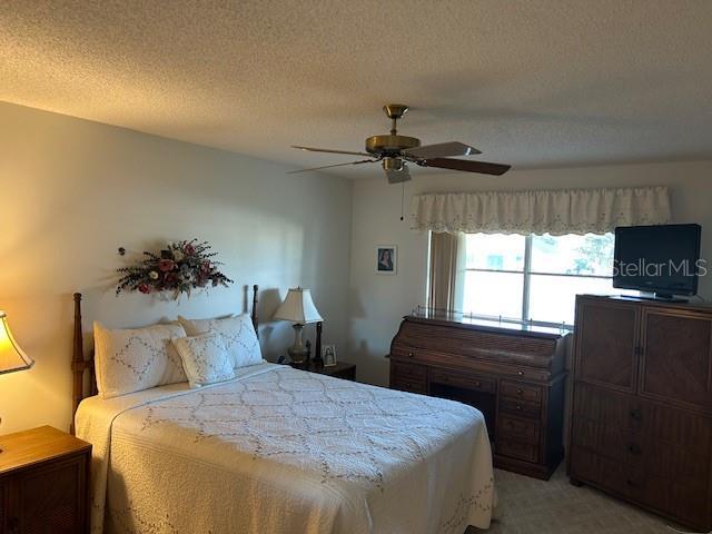 bedroom with a textured ceiling, ceiling fan, and light carpet