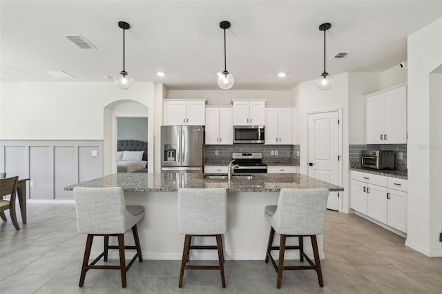 kitchen featuring dark stone countertops, white cabinetry, an island with sink, and appliances with stainless steel finishes