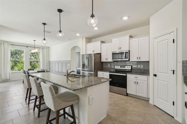 kitchen featuring appliances with stainless steel finishes, a kitchen island with sink, sink, decorative light fixtures, and white cabinets