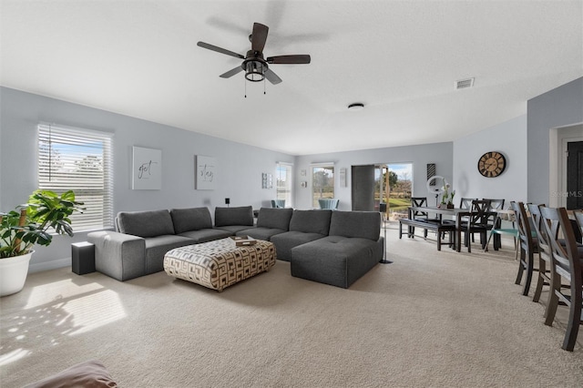 living room with a wealth of natural light, ceiling fan, and light carpet