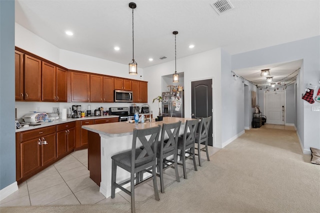 kitchen featuring appliances with stainless steel finishes, ceiling fan, decorative light fixtures, a breakfast bar area, and an island with sink