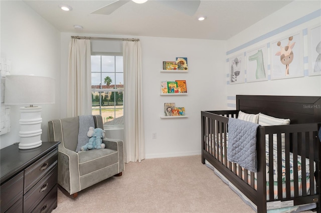 bedroom with ceiling fan, light carpet, and a nursery area