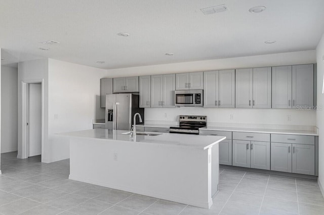 kitchen featuring gray cabinets, sink, light tile patterned floors, stainless steel appliances, and a center island with sink