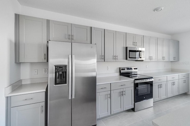 kitchen featuring light tile patterned flooring, stainless steel appliances, a textured ceiling, and gray cabinetry