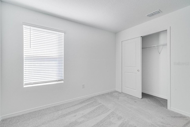 unfurnished bedroom with multiple windows, light colored carpet, a closet, and a textured ceiling