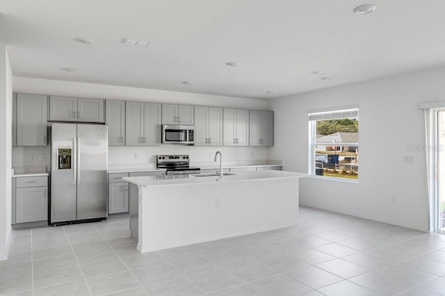 kitchen featuring appliances with stainless steel finishes, gray cabinets, a kitchen island with sink, and sink