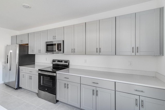 kitchen with light tile patterned floors, gray cabinets, and appliances with stainless steel finishes