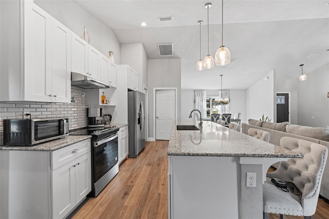 kitchen featuring white cabinets, appliances with stainless steel finishes, decorative light fixtures, and a kitchen breakfast bar