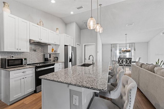 kitchen featuring white cabinets, a breakfast bar, stainless steel appliances, and an island with sink