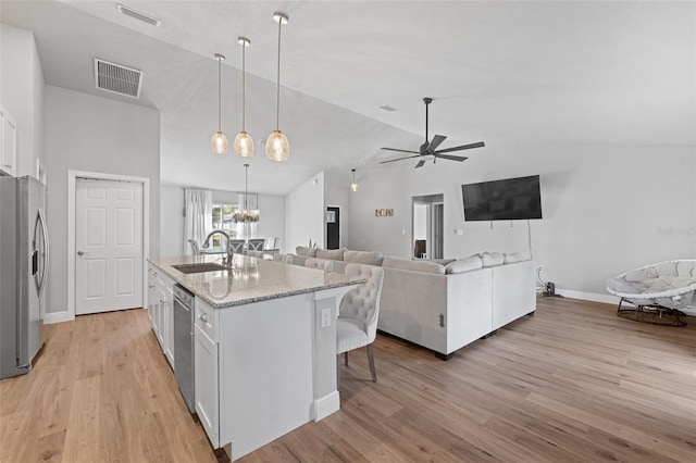 kitchen with stainless steel appliances, vaulted ceiling, a kitchen island with sink, sink, and white cabinets