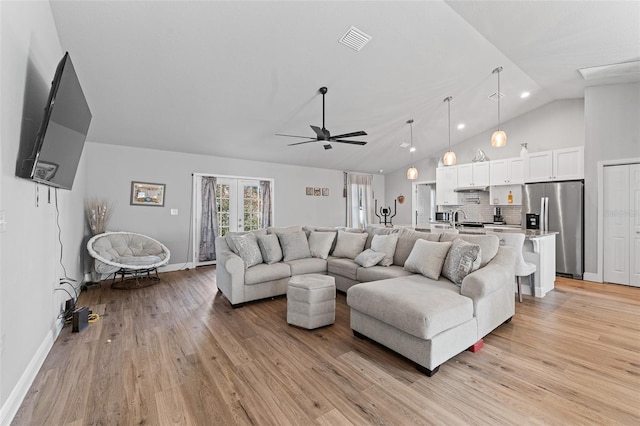 living room with ceiling fan, sink, lofted ceiling, and light wood-type flooring