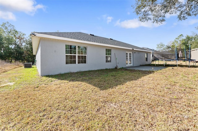 rear view of house featuring a lawn, french doors, a trampoline, cooling unit, and a patio