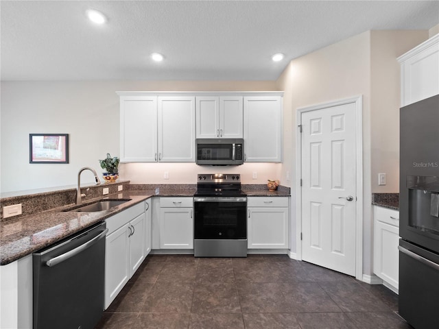 kitchen with sink, white cabinetry, dark stone countertops, kitchen peninsula, and stainless steel appliances