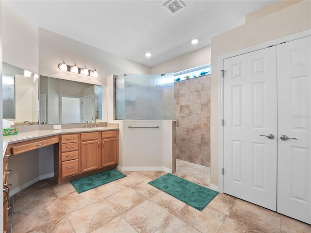 bathroom with vanity, a textured ceiling, and tiled shower