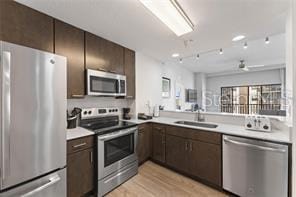 kitchen featuring kitchen peninsula, stainless steel appliances, light wood-type flooring, dark brown cabinets, and sink