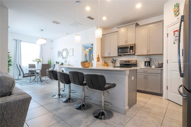 kitchen with appliances with stainless steel finishes, a kitchen breakfast bar, gray cabinetry, decorative light fixtures, and a kitchen island