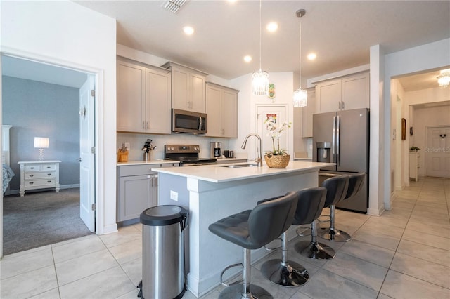 kitchen with stainless steel appliances, a kitchen island with sink, sink, decorative light fixtures, and gray cabinets