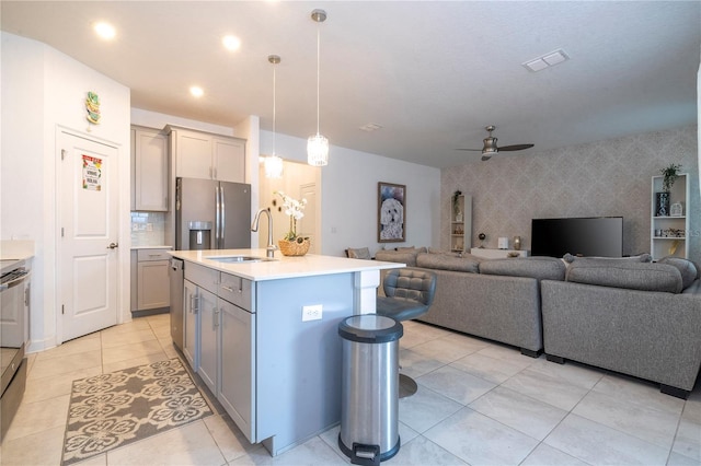 kitchen featuring a kitchen island with sink, sink, ceiling fan, appliances with stainless steel finishes, and decorative light fixtures