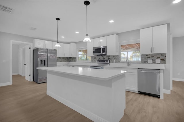 kitchen with a center island, hanging light fixtures, light wood-type flooring, white cabinetry, and appliances with stainless steel finishes